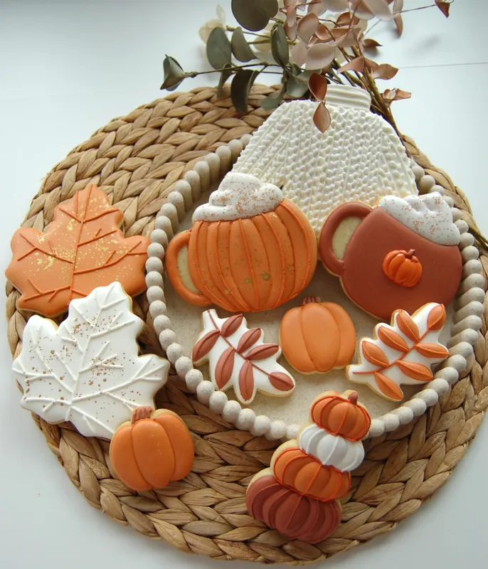 Assortiment de biscuits d’automne décorés à la main : feuilles d’érable, citrouilles et tasses sur un set en fibre naturelle