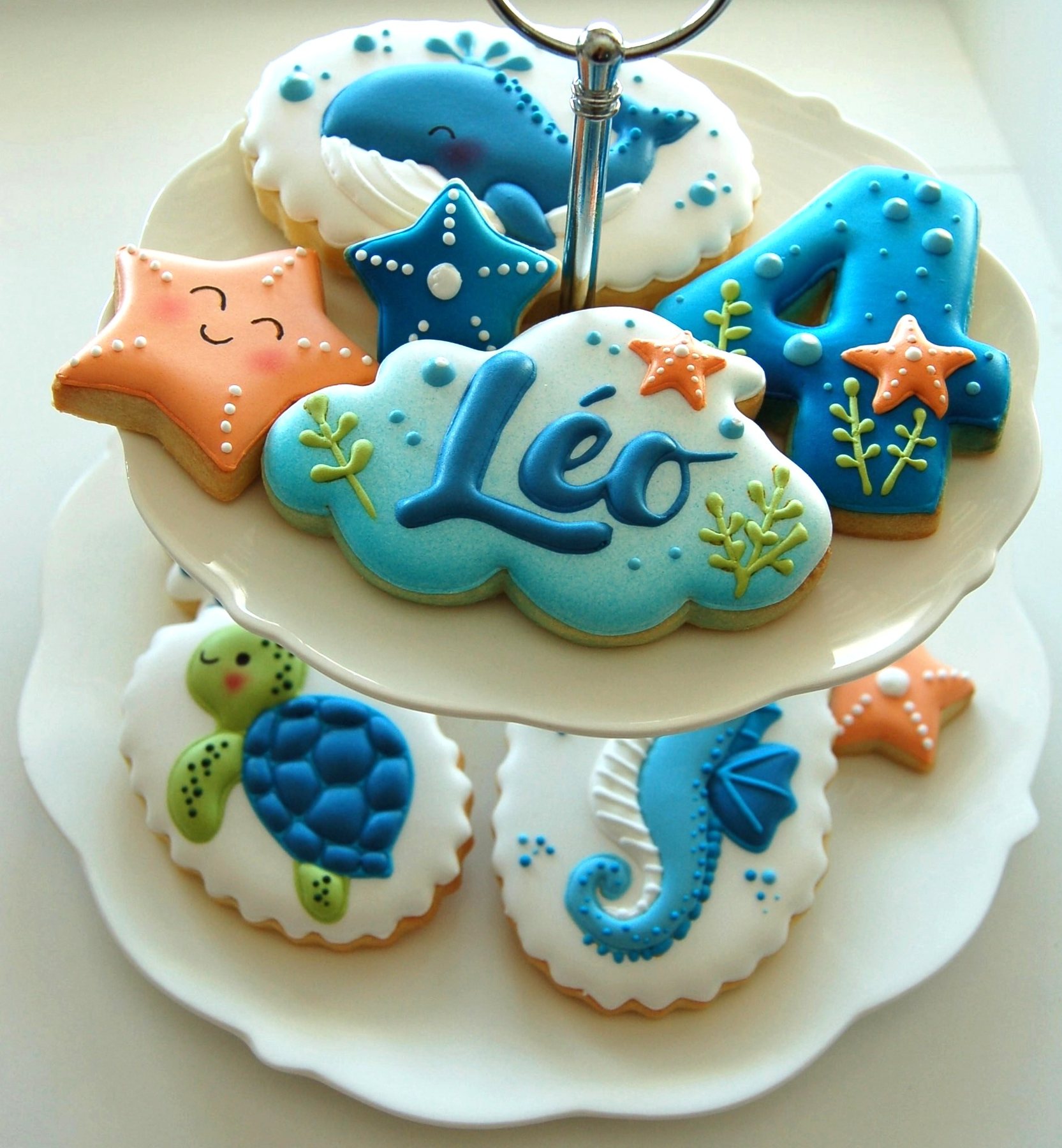 Étagère à étages garnie de biscuits décorés sur le thème de l'océan : nuage au prénom Léo, chiffre 4, tortue, hippocampe et étoiles de mer