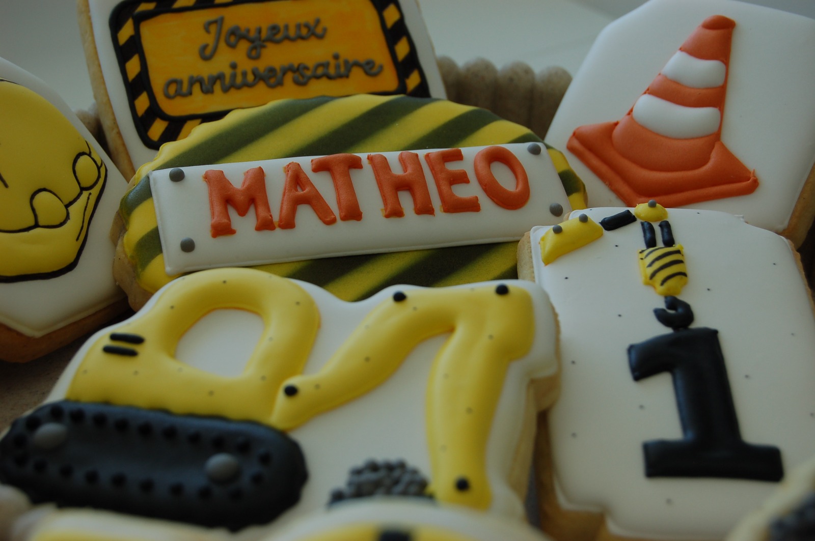 Assortiment de biscuits sur le thème du chantier : plaque au prénom Mathéo, pelleteuse, cône orange et chiffre 1