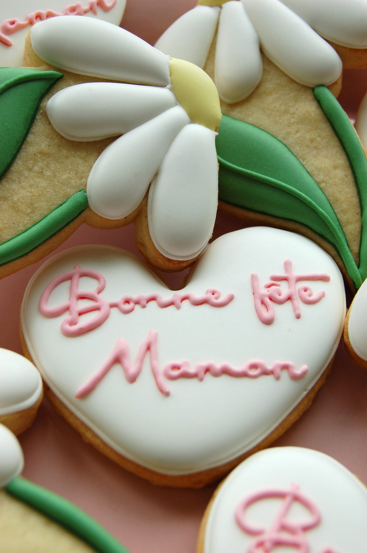 Gros plan sur un biscuit cœur Bonne fête Maman et une marguerite au cœur jaune