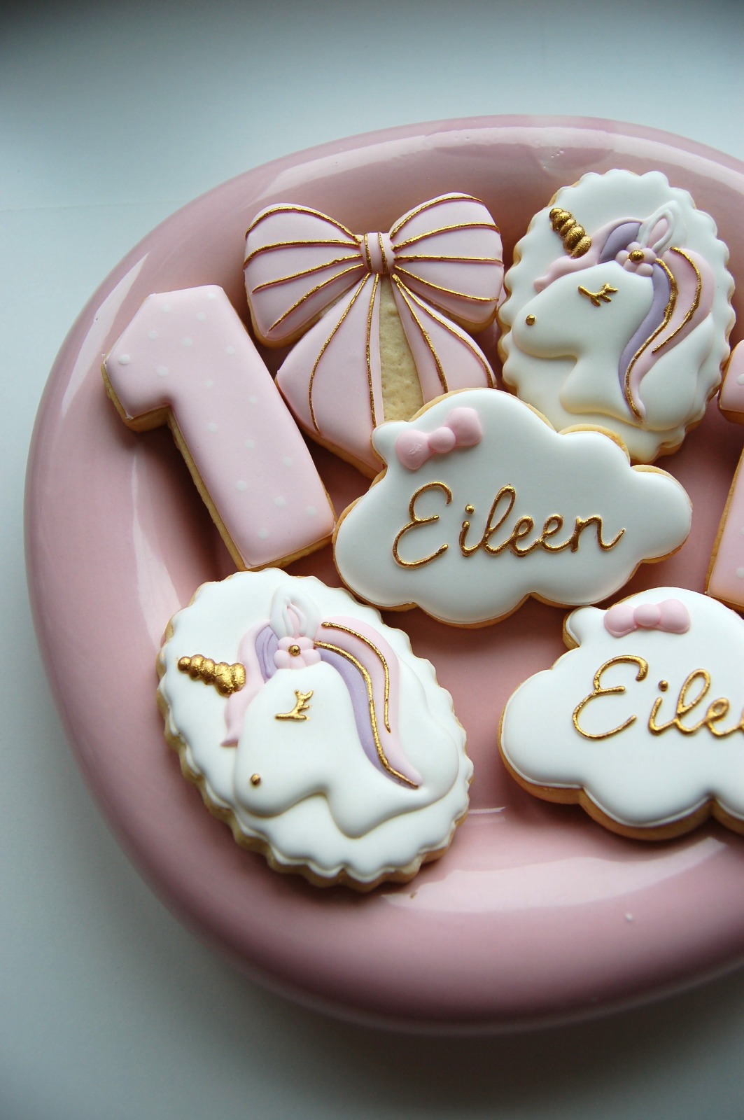 Assortiment de biscuits licorne rose et or sur une assiette : chiffre 1, nœud et nuages au prénom Eileen