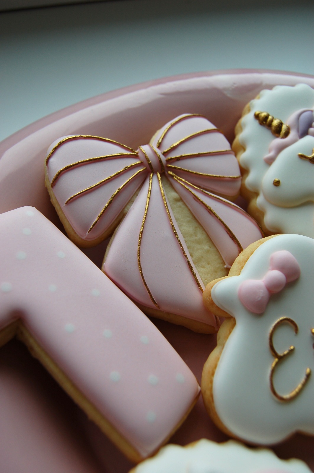 Biscuit nœud rose rehaussé de lignes dorées, entouré de biscuits licorne