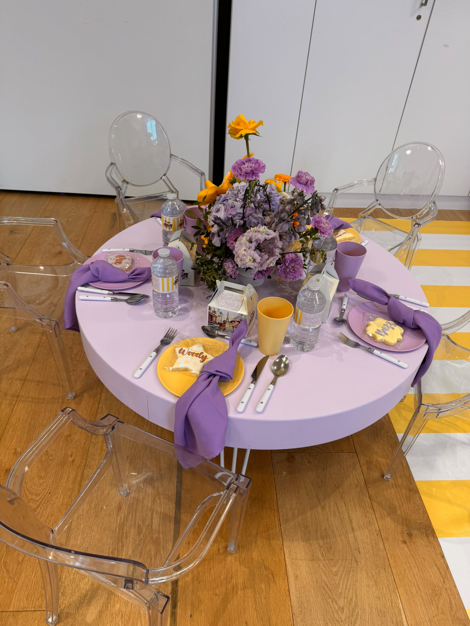 Table d'anniversaire dressée en micro-scénographie : nappe lilas, composition florale et biscuits personnalisés assortis
